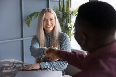 Pozitif başarılı genç sarışın iş kadını Afrikalı Amerikalı iş arkadaşıyla tokalaşıyor, çalışanıyla tokalaşıyor, mülakattan sonra işe aldığı için teşekkür ediyor, partneriyle iş birliği yapıyor.
