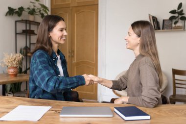 İki kadın meslektaşı ofiste el sıkışıyor, ortak görev veya projeyi başarıyla tamamlayarak birbirlerini tebrik ediyor, mesleki yardım veya destek için şükranlarını sunuyor, iş teklifini kabul ediyorlar.