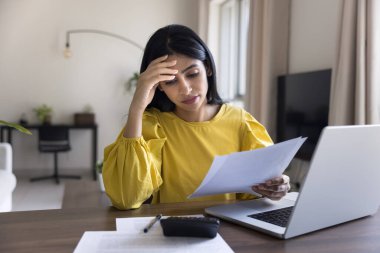 Endişeli Hintli muhasebeci kadın iş yerinde yasal mali belgeler okuyor, hesap makinesi ve dizüstü bilgisayarın üzerinde kağıt tutuyordu, kafa kafaya verip para sıkıntısı çekiyordu.