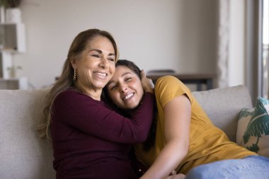 Mutlu kıdemli anne, küçük kızına şefkatle sarılıyor. Minnettarlık, sevgi, ilgi, kanepede oturuyor, başka tarafa bakıyor, gülümsüyor, yetişkin çocukla konuşuyor, anneliğin tadını çıkarıyor.