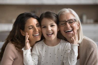 Üç kuşak kadın portresi. Anaokulu kızı, anne ve büyükanne kanepede oturur, sıcaklığın ve uyumun tadını çıkarırlar. Çok nesilli aile bağları, farklı nesiller arasındaki bağlantı