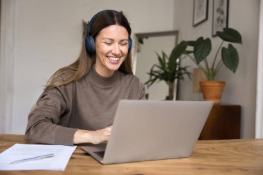 Gülümseyen güzel bir kadın masada oturur, kulaklık takar, müzik dersi dinler, e-öğrenir, yeni bilgiler edinir, eğitim platformunu kullanır, bilgisayardaki video çağrı uygulaması aracılığıyla öğretmenle konuşur.