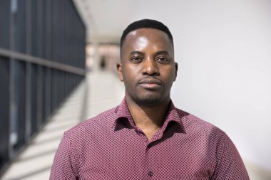Kendinden emin, yakışıklı, Afro-Amerikan iş adamı, kafasından vurulmuş. Ciddi bir genç yönetici, erkek profesyonel yalnız başına ofis koridorunda poz veriyor, resim için kameraya bakıyor.