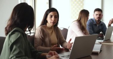 İki genç İspanyol bayan iş arkadaşı büyük bir çalışma masasında konuşuyorlar, takım çalışmasını tartışıyorlar, dizüstü bilgisayardaki iş projesini. Latin girişimci, iş kadını iş arkadaşına danışmanlık yapıyor