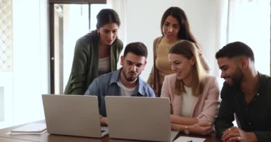 Pozitif odaklı iş ekibi birlikte laptopta online sunum izliyor, uygulamayı tartışıyor, video içeriğini tartışıyor, çalışma masasındaki iki dizüstü bilgisayarı işaret ediyor, konuşuyor