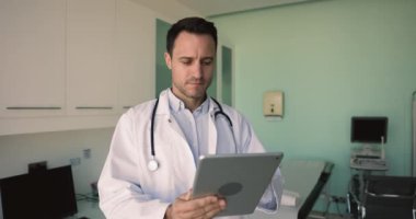 İşyerinde dijital tablet kullanan odaklanmış Latin erkek pratisyen hekim, çevrimiçi sohbetler, fikir alışverişi için iş arkadaşlarıyla kurşun yazışmalar, hastalara uzaktan profesyonel tıbbi yardım sağlama. Teknoloji