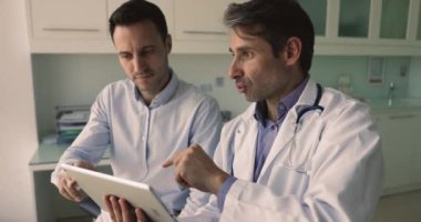 Ciddi orta yaşlı Latin pratisyen hekim terapisti hastayla konuşuyor, tablet kullanıyor, elektronik sağlık kayıtlarına erişiyor, tedavi planını güncelliyor, sağlık testi sonuçlarını gösteriyor, paylaşım tahminini sunuyor. Teknik, ilaç.