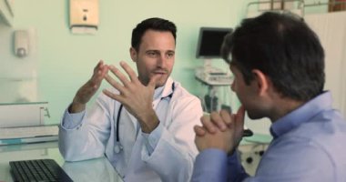 Üniformalı yetişkin İspanyol erkek pratisyen hekim, hastaneye gittiği sırada hastayla konuşuyor. Terapist ve müvekkil semptom, prognoz, ilaç tedavisi ve gelecekteki tedavi planlarını tartışıyor. Profesyonel tıbbi bakım.