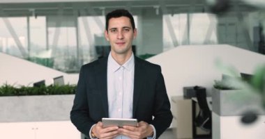 Yakışıklı genç İspanyol iş adamı açık ofis çalışma alanında portre için poz veriyor, tablet bilgisayarı tutuyor, kameraya bakıyor, mutlu oluyor, pozitif oluyor, gülüyor.