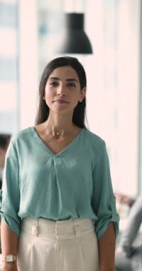 Pozitif özgüvenli şirket yöneticisi, iş kadını arkada çalışan ekiple toplantı odasında duruyor, dikey portre için poz veriyor, kameraya bakıyor, gülümsüyor, kollarını kavuşturuyor.