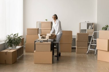 Küçük e-ticaret depolama işçisi kadın iş yerindeki konteynırları karton kutular yığınları içinde müşterilere göndermek için paketler üzerinde çalışıyor.