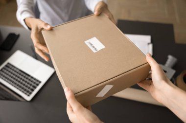 Teslimat ofisi çalışanı, depolama ofisindeki müşteriye paket veriyor, çalışma masasının üzerinde paketi tutuyor. İnternet mağazası müşterisi mağazadan satın alıyor, karton kutu alıyor