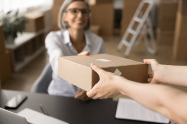 Teslimat ofisinde paket alan müşterilerin elleri. Lojistik servis yöneticisi müşteriye karton kutu veriyor, gülümsüyor, depoda oturuyor, iş yerindeki depolama odasında.