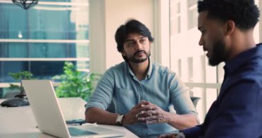 Meşgul Hintli işadamı modern ofiste dizüstü bilgisayar projesini tartışıyor. Uluslararası takım lideri ve iş arkadaşı, kurumsal toplantı odasında strateji finansmanı yönetiyor. Başarılı takım çalışması