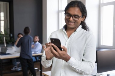 Gülümseyen orta yaşlı Hintli işadamı, ofis çalışanı, modern cihaz ya da iş yerinde gaga sırasında uygulamayı kullanarak akıllı telefon tutuyor. Yaşam tarzı, teknolojiler, elektronik hizmetler, iş konsepti