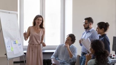 Şirket personeli konsepti için iş eğitimi etkinliği. Modern ofiste bir araya gelen çok ırklı işadamları, kendinden emin genç koçun liderliğindeki seminere parmak şıklatma grafiğinde sunum yaptı.