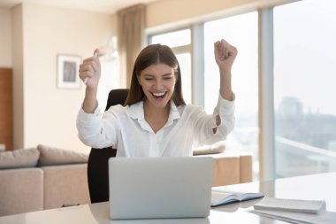 Kariyerini ilerlet, terfi et, büyük bir ticari teklif al, internet piyangosunu kazan, zafer kazan. Genç neşeli kadın dizüstü bilgisayarla masada oturuyor, e-posta okuyor iş başarısını kutluyor mutlu ol.