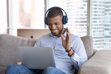 Mutlu Afrikalı bir selamlama arkadaşı, iş arkadaşı ya da internetteki özel öğretmen video konferansı için kanepede dizüstü bilgisayarla oturuyor. Çalışma ya da öğrenim tarafından sanal toplantı, modern teknoloji kullanılarak kişisel iletişim