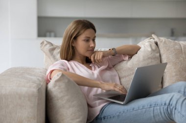 Ciddi düşünceli bir kadın evdeki kanepede dizüstü bilgisayarla elektronik alışveriş yapıyor, yeni yazılımlar kazanıyor düşünceli görünüyor, internette sohbet ediyor, mal satın alıyor, internetten sipariş veriyor. Modern teknoloji, eğlence.