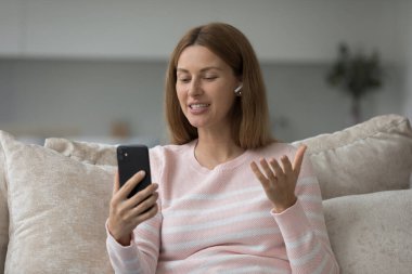 Kulaklıklı genç bir kadın sanal toplantı yapıyor, yurtdışında yaşayan bir arkadaşına ya da ailesine video konferansı hazırlıyor, evdeki kanepede oturuyor. Uzak iletişim için modern kablosuz teknoloji kullanımı, mobil uygulama