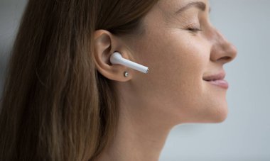Güzel, gülümseyen bir kadın kaliteli sesten ve kulaklıkla en sevdiği şarkıdan hoşlanır, profil yüz görüntüsünü kapatır. Hobi ve eğlence için dijital müzik hizmetleri, modern kablosuz teknolojiler