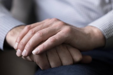 Elleri üst üste dizilmiş, avuç içleri manikürlü, bilekleri kucağında, endişeli, endişeli, vücut hareketlerini bekleyen, kaygılı yaşlı bir adam. Yaklaş, kırpılmış atış.