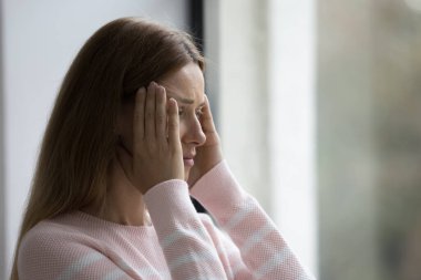 Kapalı yerde duran genç kadın şiddetli baş ağrısı, kronik migren, yüksek tansiyon, acı veren duyguları yatıştırmak için masaj tapınakları, stresli bir durumdan dolayı hasta ya da kötü görünüyor.