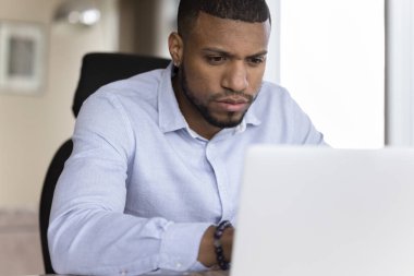 İşyerinde laptopla çalışan odaklanmış Afrikalı işadamı, kapat. Meşgul Amerikalı girişimci bilgisayar ekranına bakıyor, çözümü düşünüyor, çevrimiçi projeye hazırlanıyor, yeni yazılım öğreniyor