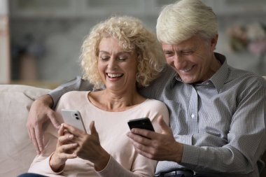 Mutlu koca ve eş akıllı telefon tutuyor, mesajlar okuyor, çevrimiçi oyunlar oynuyor, ekranlara bakıyor, gülüyor, video konferans görüşmesinde konuşuyor, uygulama kullanıyor, internet iletişiminden keyif alıyor.