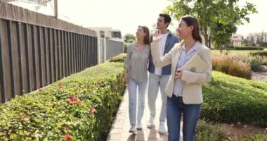 Kendine güveni tam bir emlakçı varoş mahallesinde müşterilerle yürüyor, çit kapısı açıyor, kiracıları avluya ve kiralık konutlara davet ediyor, satılık eve geliyor, kira ödüyor.