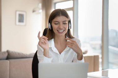 Kablosuz kulaklıklı mutlu kadın evde video görüşmesi yapıyor, online şirket konferansında projeyi tartışıyor, dizüstü bilgisayarımda oturuyor, bilgisayar kamerasında konuşuyor.