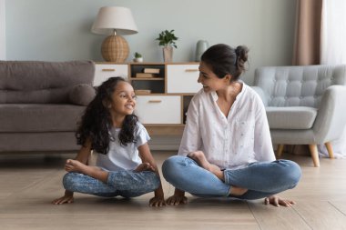Mutlu Hintli anne ve kız evde yoga yapıyor, asma sana asıyor, bacak bacak bacak üstüne atmış Lotus pozuyla kol dengesini koruyor, ellerinde uydu bedenlerini kaldırıyor. Pul, Tolasana, Utpluthi