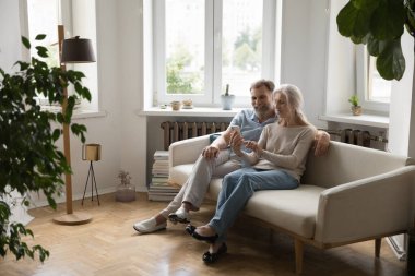 Yeni iç mekanda koltukta oturan mutlu yaşlı çift, cep telefonunda internet uygulaması kullanıyor, internetten alışveriş yapıyor, cihazları paylaşıyor, video konuşmaları yapıyor. İletişim, emeklilik