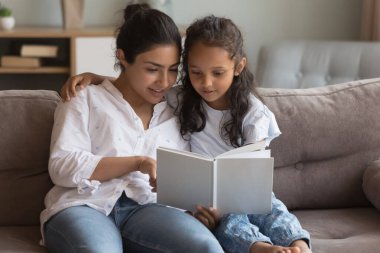 Mutlu genç Hintli anne küçük kızına kitap okumayı öğretiyor, ilkokul ödevlerine yardım ediyor, resimler gösteriyor, peri masalı anlatıyor. Anne ve kız rahat koltukta dinleniyor.