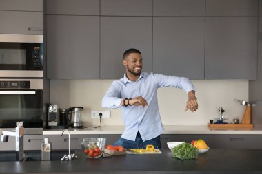 Neşeli Afrikalı aşçı blogcu adam mutfakta müzik eşliğinde dans ediyor, mutfak hobisinin tadını çıkarıyor, organik gıda malzemelerinden salata hazırlıyor, taze sebzeler pişiriyor, eğleniyor, gülüyor.