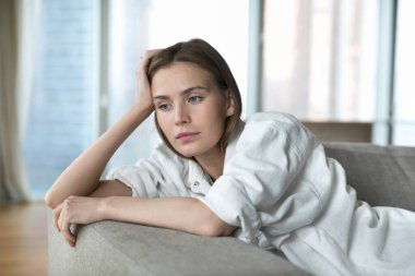 Close up sad young 25s attractive woman, brooding, deep in thoughts, resting on sofa, thinking about personal life concerns, goes through break up with boyfriend, marriage split, bored alone at home clipart