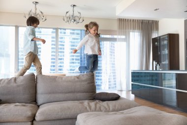 İki küçük şirin kardeş, anaokulu çocuğu ve kız gündelik giysiler içinde modern oturma odasında birlikte eğleniyorlar, oyun oynuyorlar, oynuyorlar, koşuyorlar, modern evdeki rahat yumuşak koltukta zıplıyorlar. Oyun zamanı, çocukluk