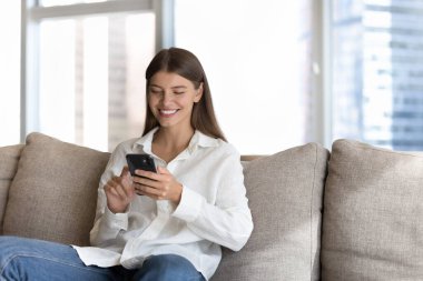 Neşeli, 20 'li yaşlardaki güzel bir kız cep telefonuyla yazı yazıyor, şehirdeki evdeki koltukta oturuyor internet iletişiminin keyfini çıkarıyor, ekranlara dokunuyor, finansal ekommerce uygulaması kullanıyor.