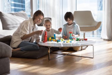 Mutlu genç anne evde küçük çocuklarla rahatlar, renkli ahşap bloklardan kale yapılmasına yardım eder, oturma odasında oturur, çocukları geliştirir, kızlarıyla ve oğluyla eğlenirken yaratıcı oyunlardan zevk alır.