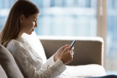 Evinde cep telefonuyla yazan, uygulamayı, sanal servisi, yazılımı, dijital aygıtı kullanan, gerçekten güzel bir genç kadın. Yan görünüm