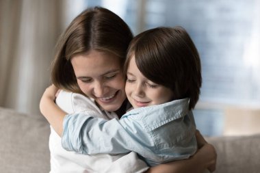 Yakından çekilen genç anne, sevimli beşli yaşlarındaki oğluna sıkıca sarılıyor sevgi dolu bir aile, gözleri kapalı kucaklaşmanın tadını çıkarıyor ve evde birlikte vakit geçiriyorlar. Anneler Günün kutlu olsun, annelik, terbiye, koşulsuz sevgi