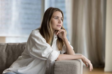 Pozitif rüya gibi güzel bir kadın rahat bir kanepede dinleniyor, çenesine dokunuyor, derin, hoş düşüncelerle yüzünü çeviriyor, gülümsüyor, düşünüyor, hayal kuruyor, rahat, modern dairede keyfine bakıyor. Rahatlama