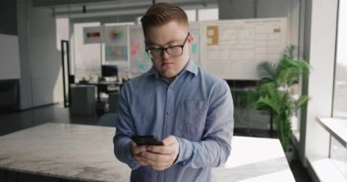 Down sendromlu bir adam akıllı telefonu modern iş yerinde tutar, görevleri yönetir, günlük programı düzenlemek için uygulamalar kullanır, hatırlatıcıyı ayarlar, işle ilgili mesajlara cevap verir, iş arkadaşlarıyla güncellemeleri paylaşır