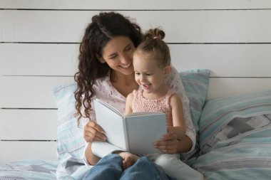 Okuma maceraları. Aile portresi, özenli anne, küçük okul çocuğu kız çocuk birlikte evde kaliteli zaman geçirir yatakta kitap okur popüler çocuk yazarlarının yeni peri masalı romanlarının keyfini çıkarırız.