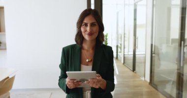 Dijital tablet tutan, modern çalışma alanında duran zarif ceketli mutlu Latin iş kadınının ofis portresi, kameraya bakıyor, profesyonellik, yetenek ve başarı yayıyor. Kariyer