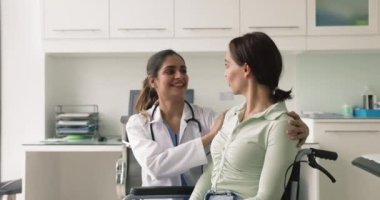 Mutlu genç Hintli doktor engelli kadın hastaya destek ve umut veriyor, tekerlekli sandalyedeki kadının omzuna dokunuyor, iyi haberler veriyor, başarılı terapi sonuçları veriyor.