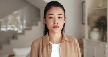 Ciddi genç Asyalı kadın kameraya bakıyor, evde portre için duruyor, elini uzatıyor ve avuç içini gösteriyor, duruyor, fotoğraf makinesinden koluna doğru hareket eden reddedilme hareketi yapıyor.