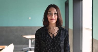 Ofiste portre için poz veren Avrupalı özgüvenli iş kadını, kameraya bakıyor, mutlu oluyor, gülümsüyor, beyaz dişlerini açıyor, güven jesti olarak kollarını göğsünde kavuşturuyor.