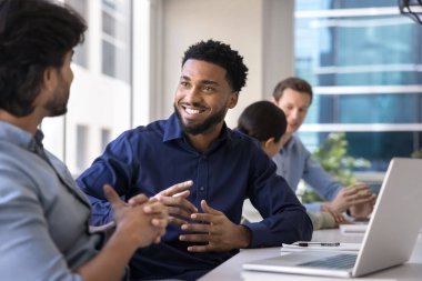 Yakışıklı Afro-Amerikan proje yöneticisi erkek Hintli meslektaşıyla büyük çalışma masasında buluşuyor, iş arkadaşlarıyla konuşuyor, gülümsüyor, gülüyor, iş iletişiminden keyif alıyor, iletişim kuruyor.