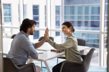 İki mutlu Hintli genç iş arkadaşı beşlik çakıyor başarılı bir işbirliğini simgeliyor ortaklık, iş arkadaşlığı, iyi bir takım çalışmasının sonucunu kutlamak, uzlaşma sağlamak, gülümsemek, gülmek.